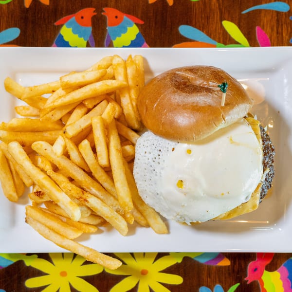 Burger with a fried egg and a side of golden french fries on a white rectangular plate.