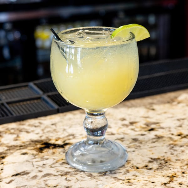 Margarita in a goblet glass with ice, lime, and straw on a speckled bar counter.