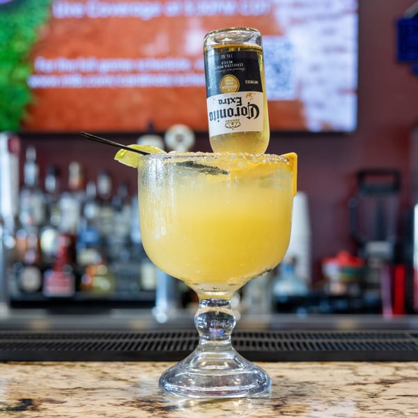 Coronarita drink with a Corona Extra bottle inverted into a salted margarita glass on a bar.
