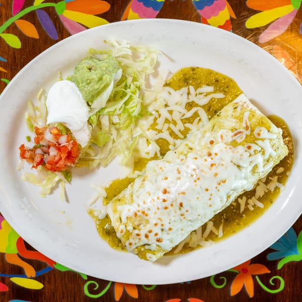 A cheesy green chile burrito served with shredded lettuce, guacamole, sour cream, and fresh pico de gallo.