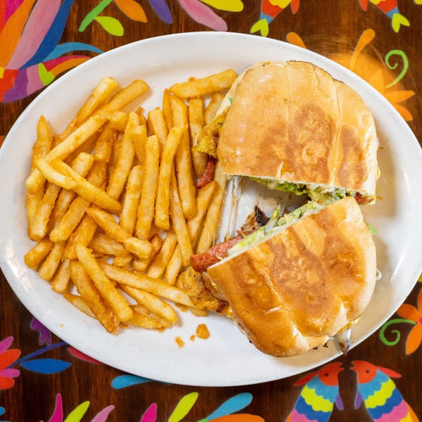 Sandwich cut in half with fries on a white plate, set on a colorful patterned table.