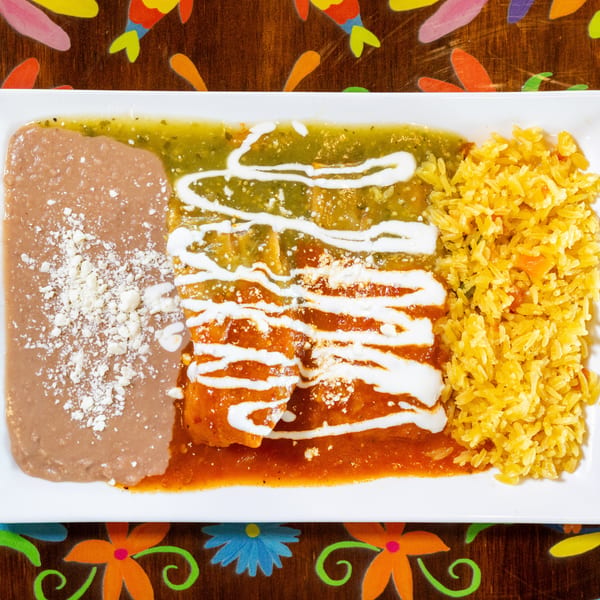 Enchiladas with red and green sauce, drizzled with sour cream, served with refried beans and yellow rice.