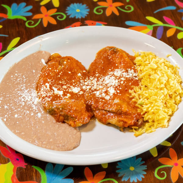 Two red-sauced entrees with cotija cheese, refried beans, and yellow rice on a white plate.