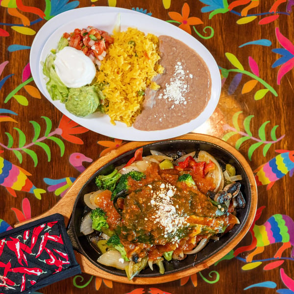 Mexican combo plate and sizzling chile relleno with vegetables on a vibrant, patterned table.