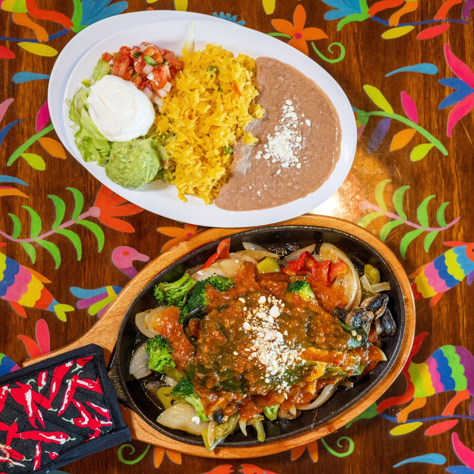 Mexican combo plate and sizzling chile relleno with vegetables on a vibrant, patterned table.
