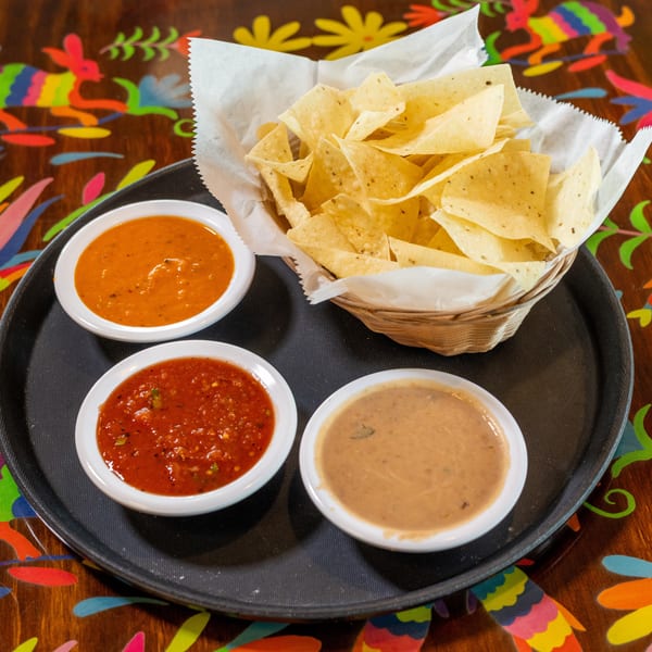 Crispy tortilla chips with red salsa, orange salsa, and bean dip on a vibrant table.