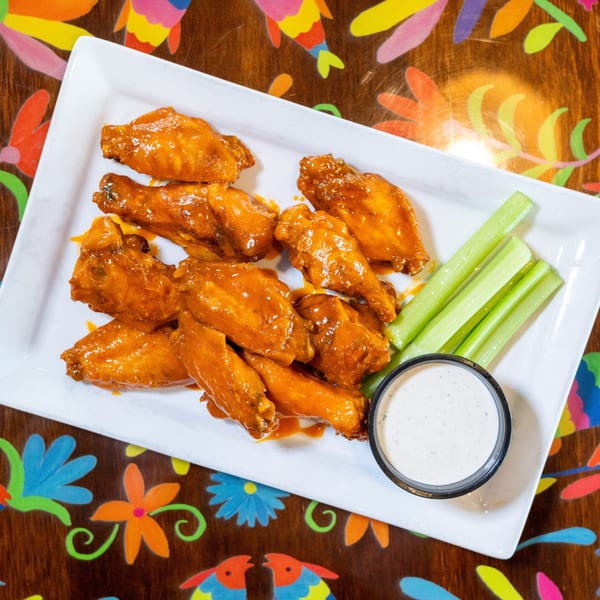 Orange glazed chicken wings with celery sticks and ranch dip on a white plate.