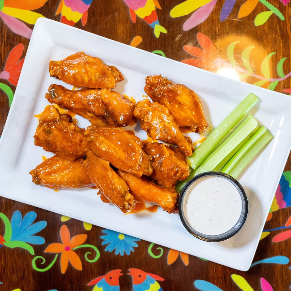 Orange glazed chicken wings with celery sticks and ranch dip on a white plate.