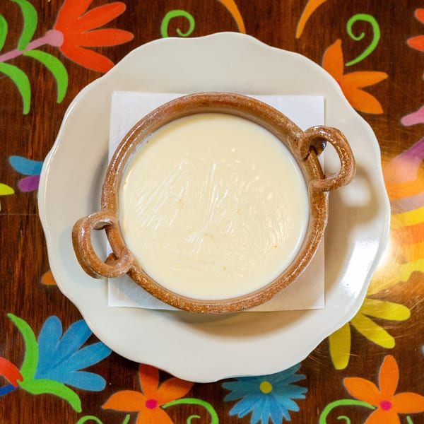 Creamy white queso in a rustic terracotta bowl on a vibrant, folk-art patterned table.
