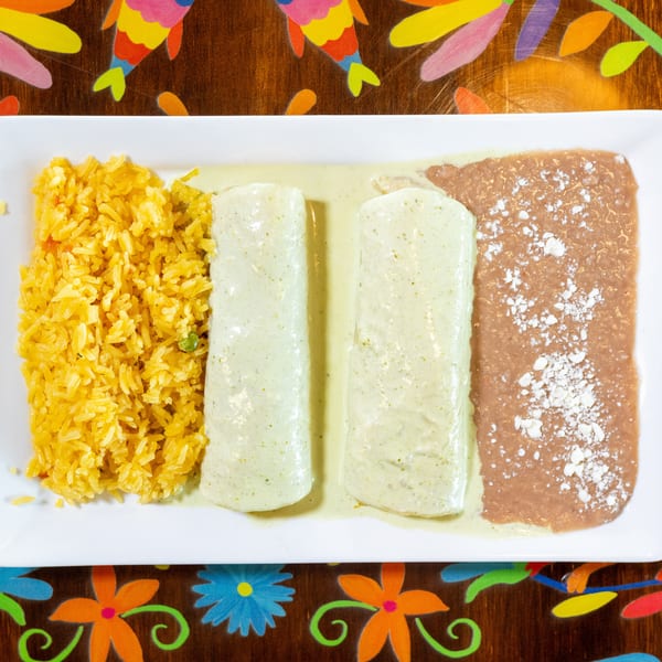 Plate of yellow rice, two enchiladas with green sauce, and refried beans with cheese.