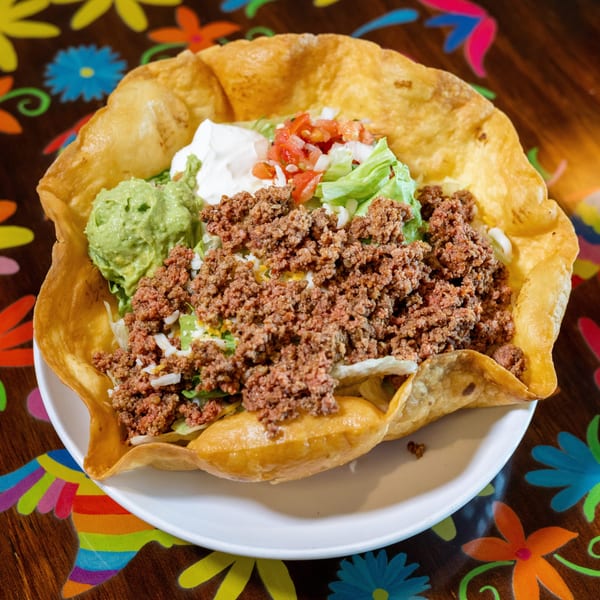 Taco salad in a crispy tortilla bowl with ground beef, guacamole, sour cream, and pico de gallo.