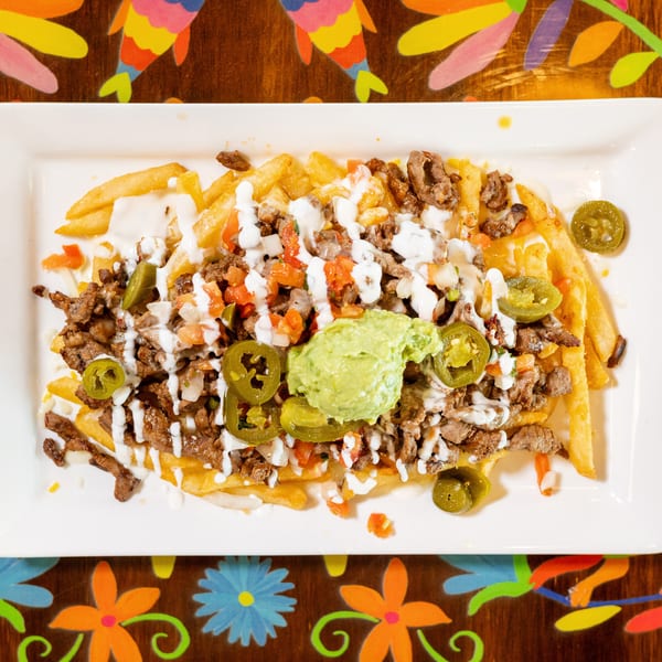 Loaded french fries with steak, guacamole, pico de gallo, jalapeños, and white sauce on a festive table.